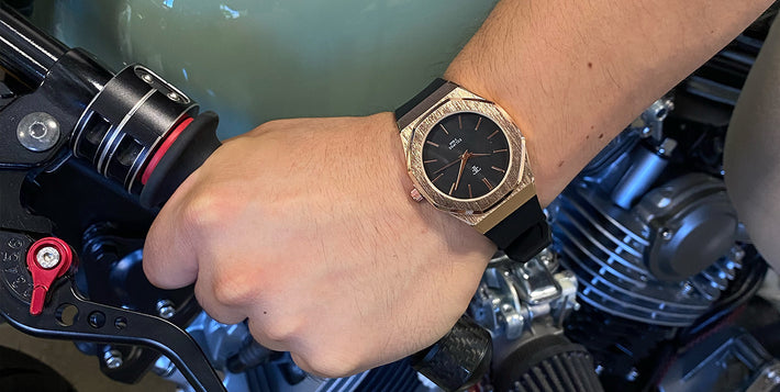 A hand wearing a gold watch grips a motorcycle throttle.
