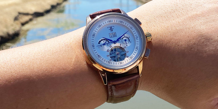Wristwatch with a gold case and brown leather strap, worn outside in sunlight.